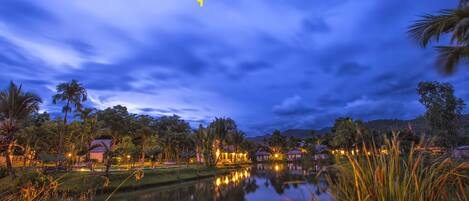 A nighttime view of a lakeside area with buildings and palm trees.
