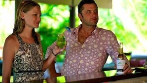 Two people standing at a bar with a green outdoor background. - Crab Claw Island (Bynoe)