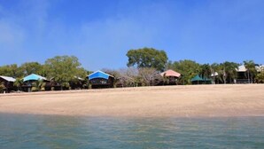 A beachfront property with multiple structures, including a main building and several smaller huts, surrounded by trees and a sandy beach. - Crab Claw Island (Bynoe)