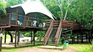 A covered outdoor seating area with a staircase leading up to it, surrounded by trees. - Crab Claw Island (Bynoe)