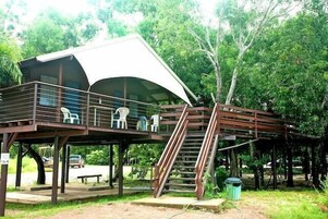 A covered outdoor seating area with a staircase leading up to it, surrounded by trees.