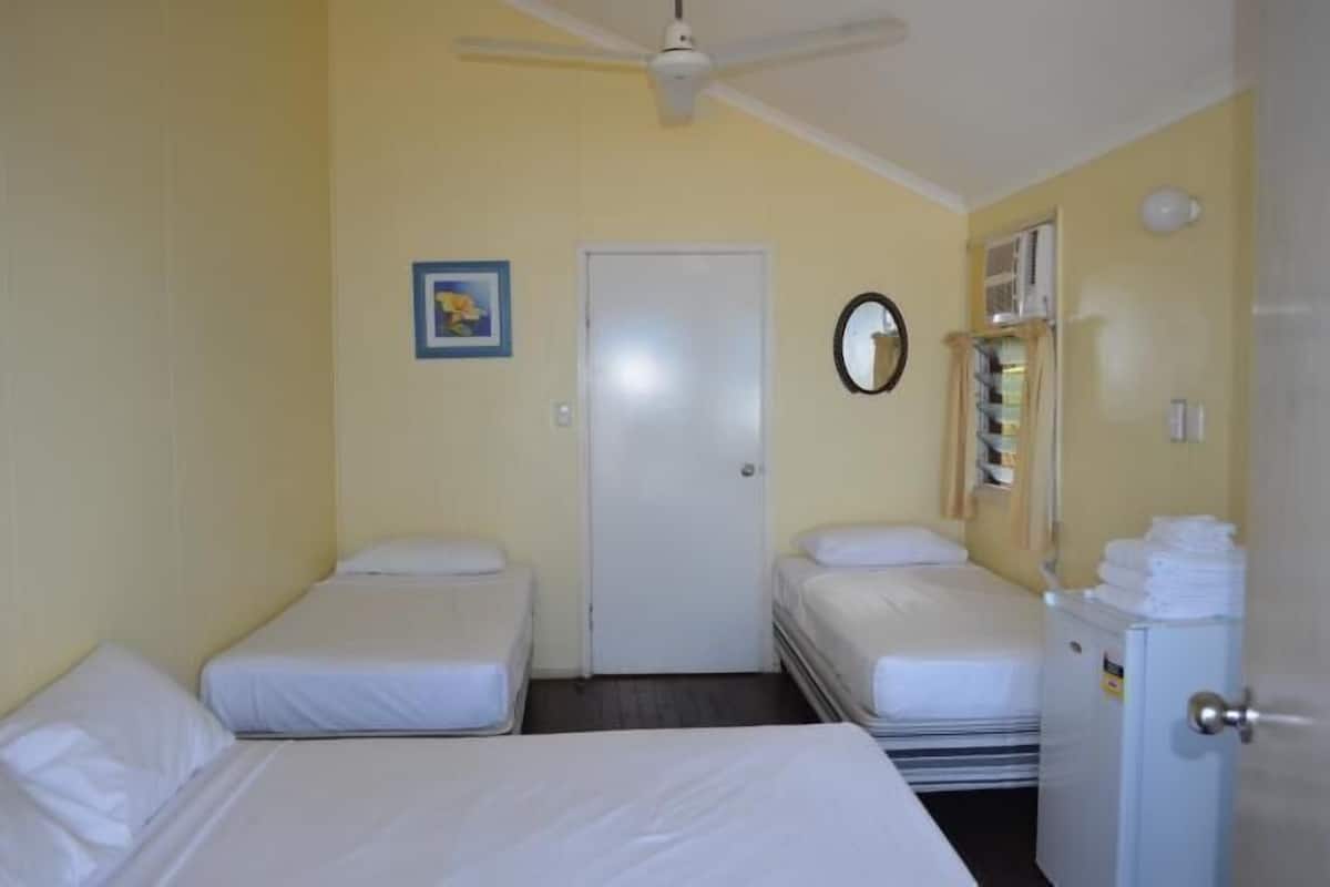 A room with two single beds, a ceiling fan, a door, a mirror, and a small refrigerator.