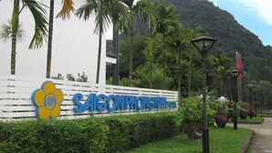 Schild für "SAGONPHONEN" mit Logo, umgeben von Grünpflanzen und einem Berg im Hintergrund.