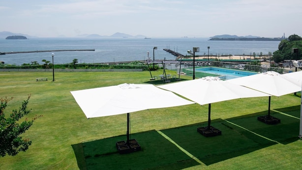 A grassy area with white umbrellas and a swimming pool. - Kurashiki Seaside Hotel (Kurashiki)