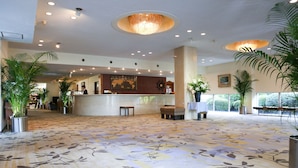 A spacious lobby with a floral carpet, a reception desk, and several potted plants. - Kurashiki Seaside Hotel (Kurashiki)