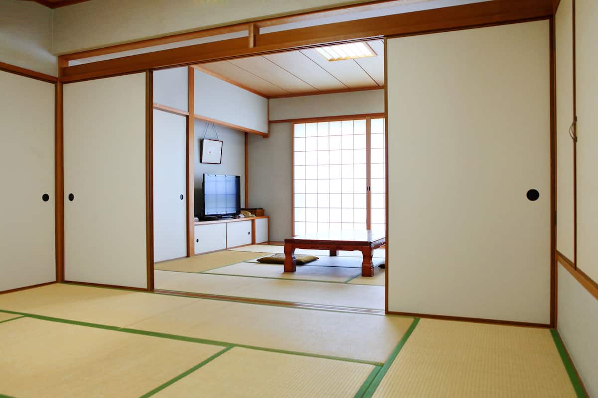 Quarto japonês tradicional com tatames, portas deslizantes, uma televisão e uma pequena mesa.