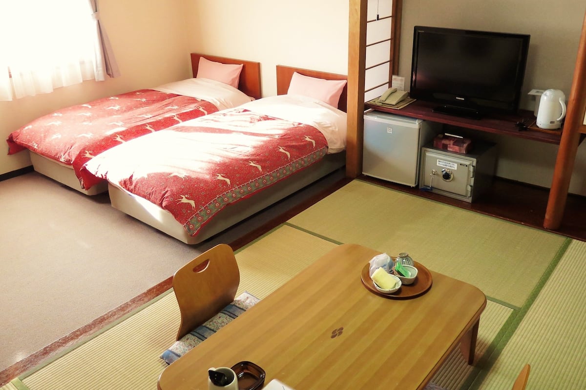 Une chambre d’hôtel avec deux lits, une télévision, un petit réfrigérateur et une table basse de style japonais, accompagnée d’un service à thé.