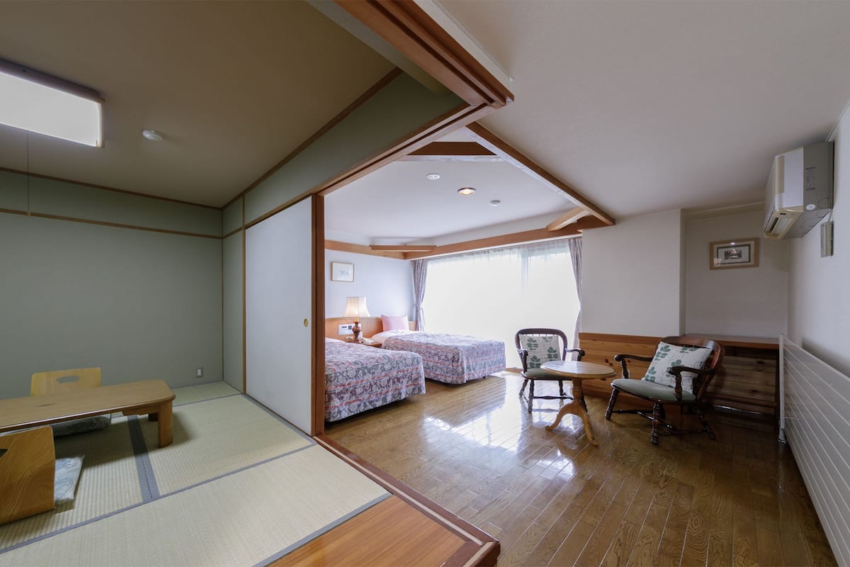 Une pièce de style japonais traditionnel, avec un sol recouvert de tatamis, un plafond bas en bois et une porte coulissante donnant sur une autre pièce.