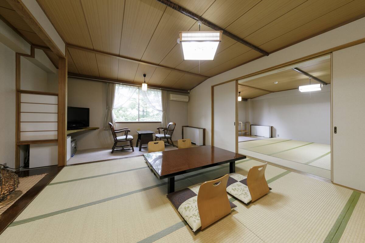 Une pièce traditionnelle avec un sol recouvert de tatamis, une table basse en tatami, des meubles bas en bois et un téléviseur.
