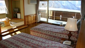 A hotel room with two beds, a desk, a chair, a TV, and a large window with a view of snow-covered mountains. - Hotel White Inn Kitashiga (Yamanouchi)