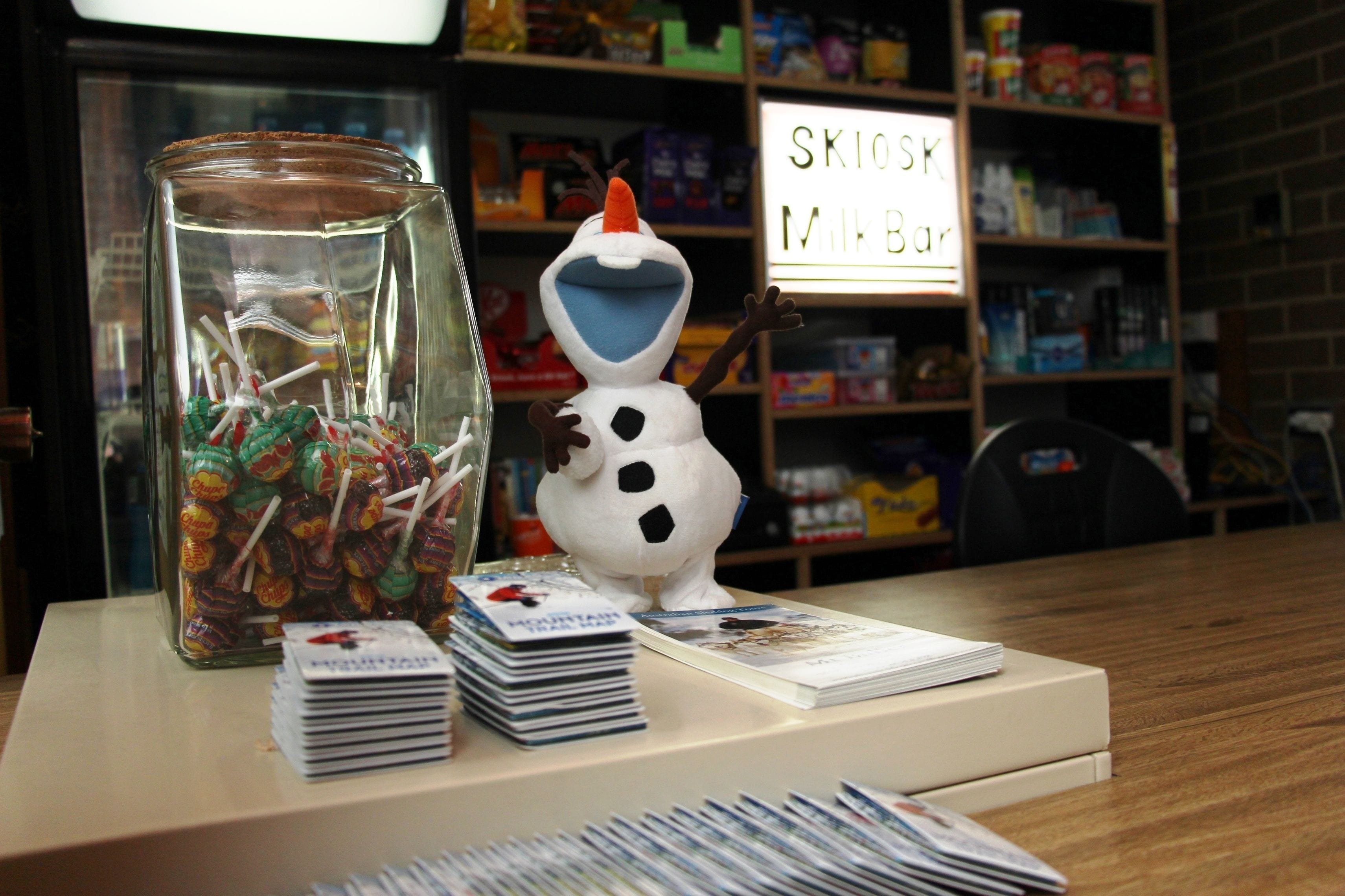Un frasco de vidrio lleno de piruletas de colores, una figura de muñeco de nieve y pilas de revistas sobre una mesa.