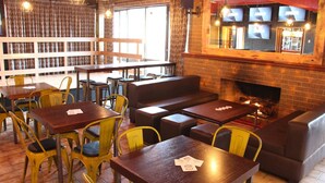 A cozy restaurant with wooden tables and yellow chairs, a brick fireplace, and a large window. - Alpine Retreat Mt Buller (Mount Buller)