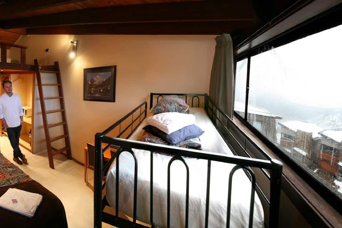 A bedroom with a bunk bed, a single bed, a ladder, and a window with a view of a snowy landscape.