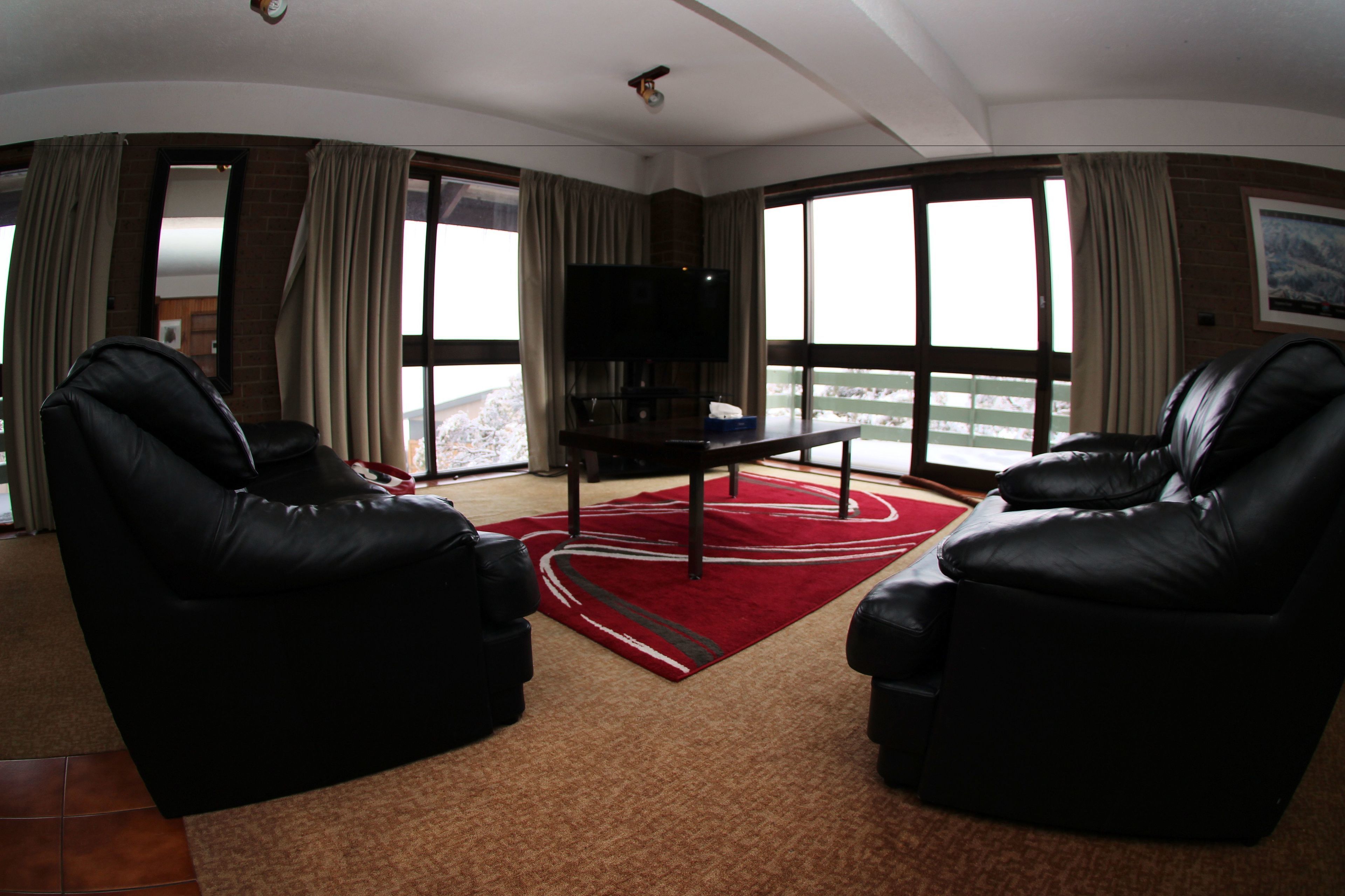 A spacious living room with two black leather sofas, a flat-screen TV, and a red carpet.
