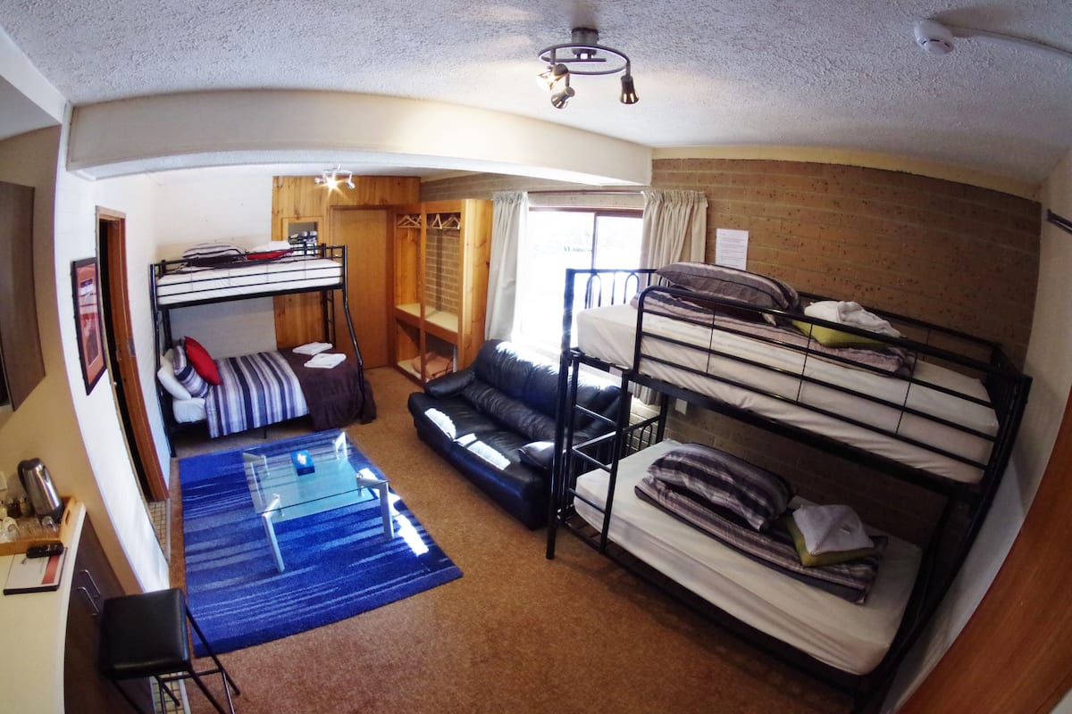A compact room with bunk beds, a sofa, a small table, and a desk with a chair.