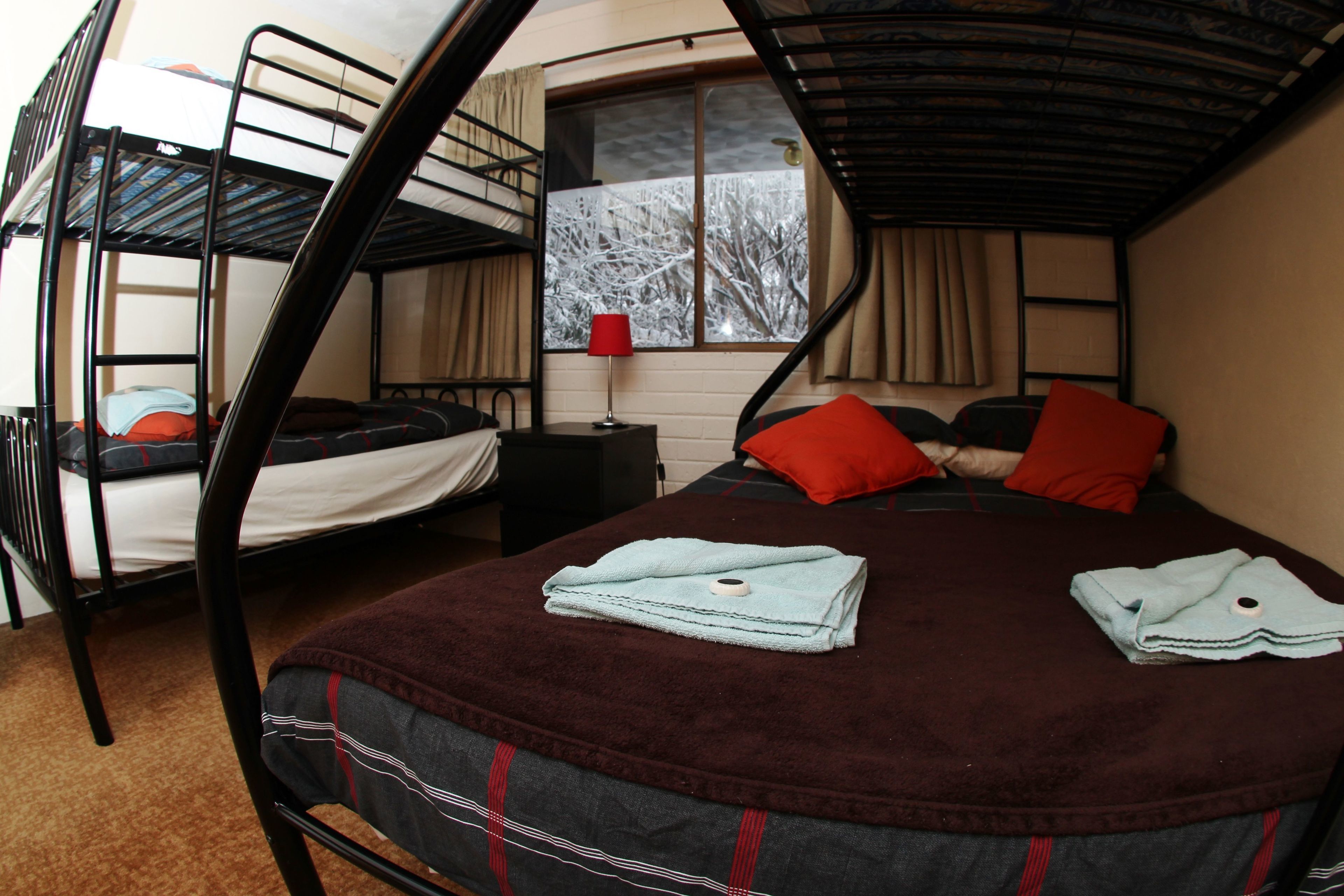 Un dormitorio con literas, una ventana con vistas a árboles y una lámpara roja sobre una mesita de noche.