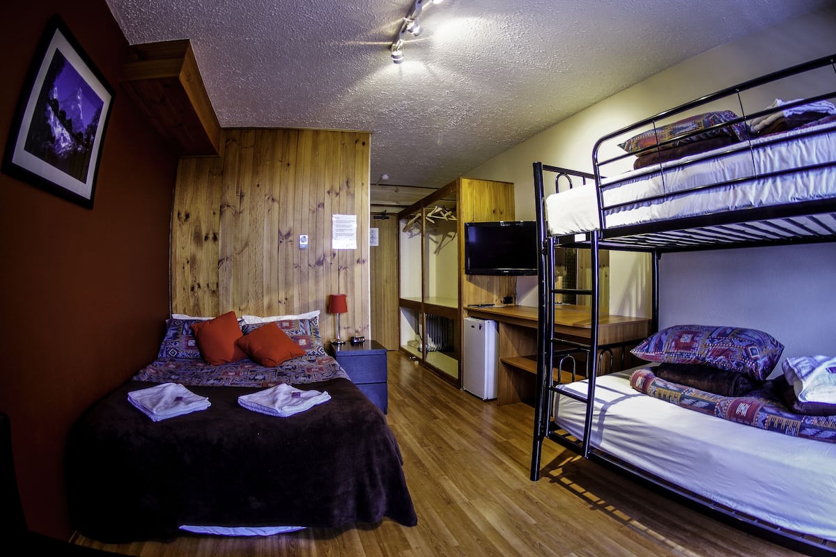 A room with a bed, a desk, a TV, and a bunk bed.