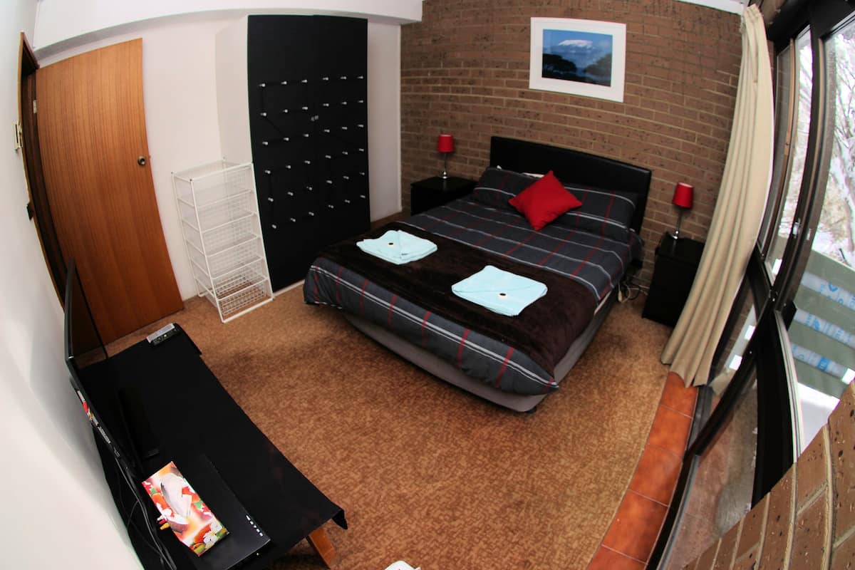 A bedroom with a bed, a desk, a wardrobe, and a window.