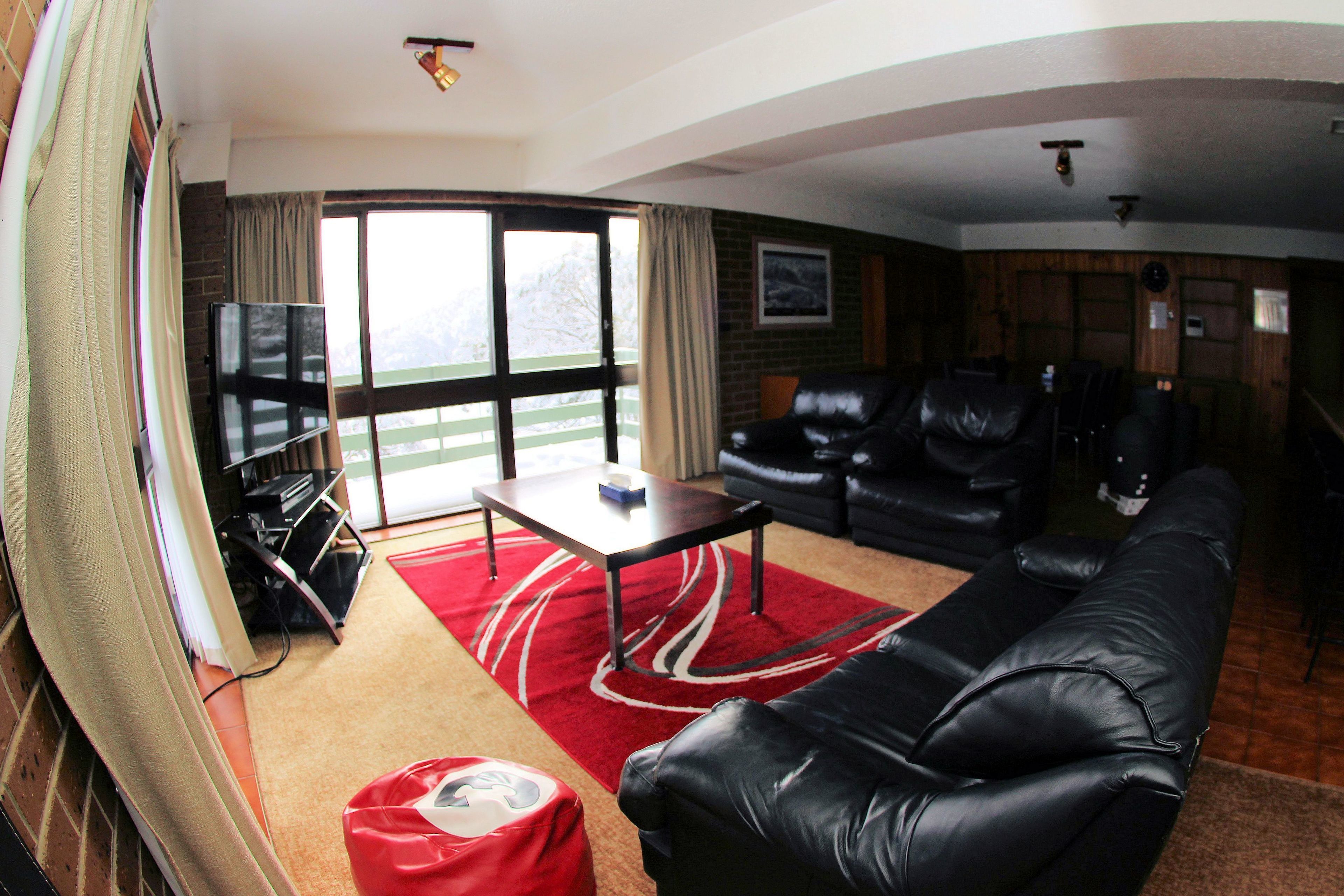 A living room with a black leather sofa, a red rug, a small table, and a TV.