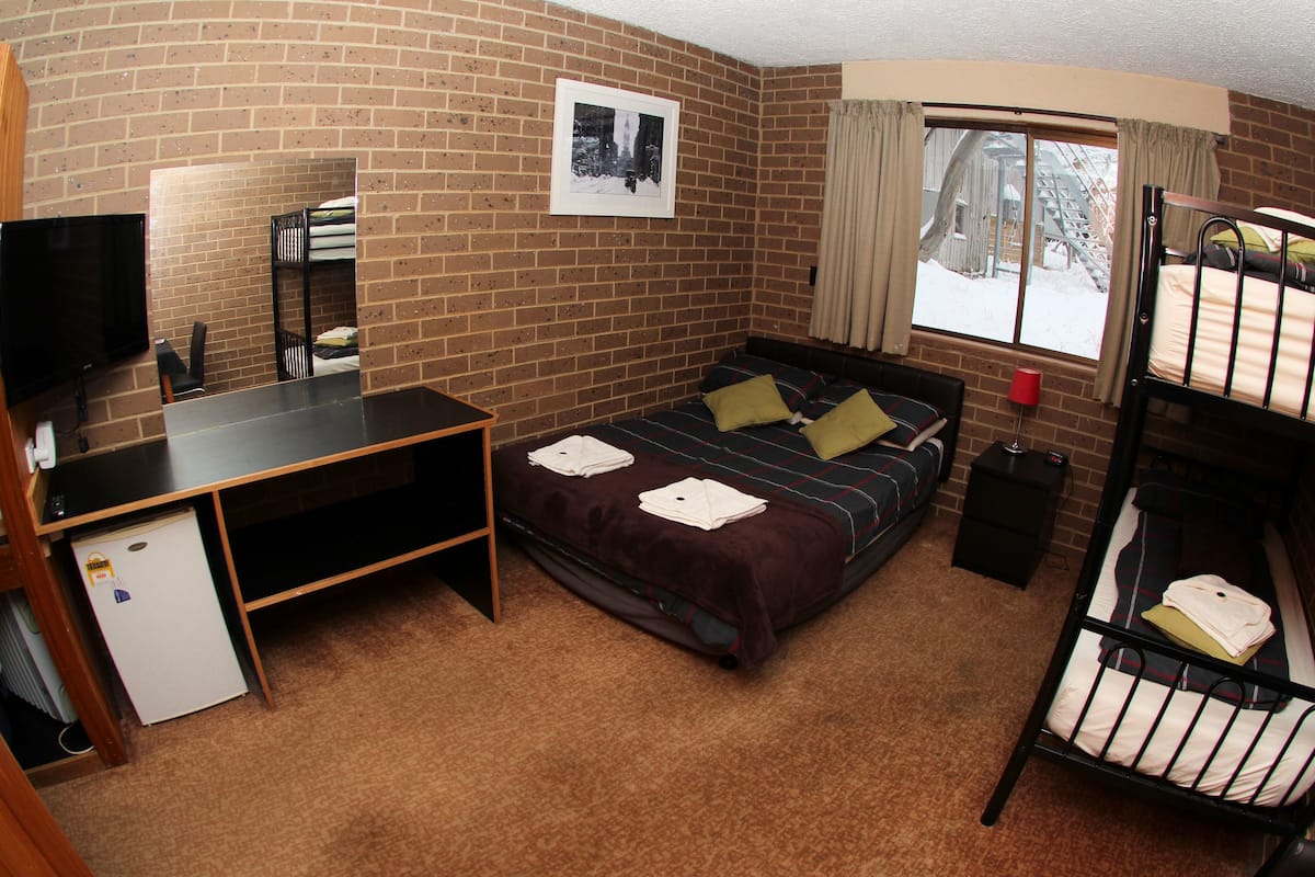 A room with a bunk bed, a desk with a computer, a television, and a window with curtains.