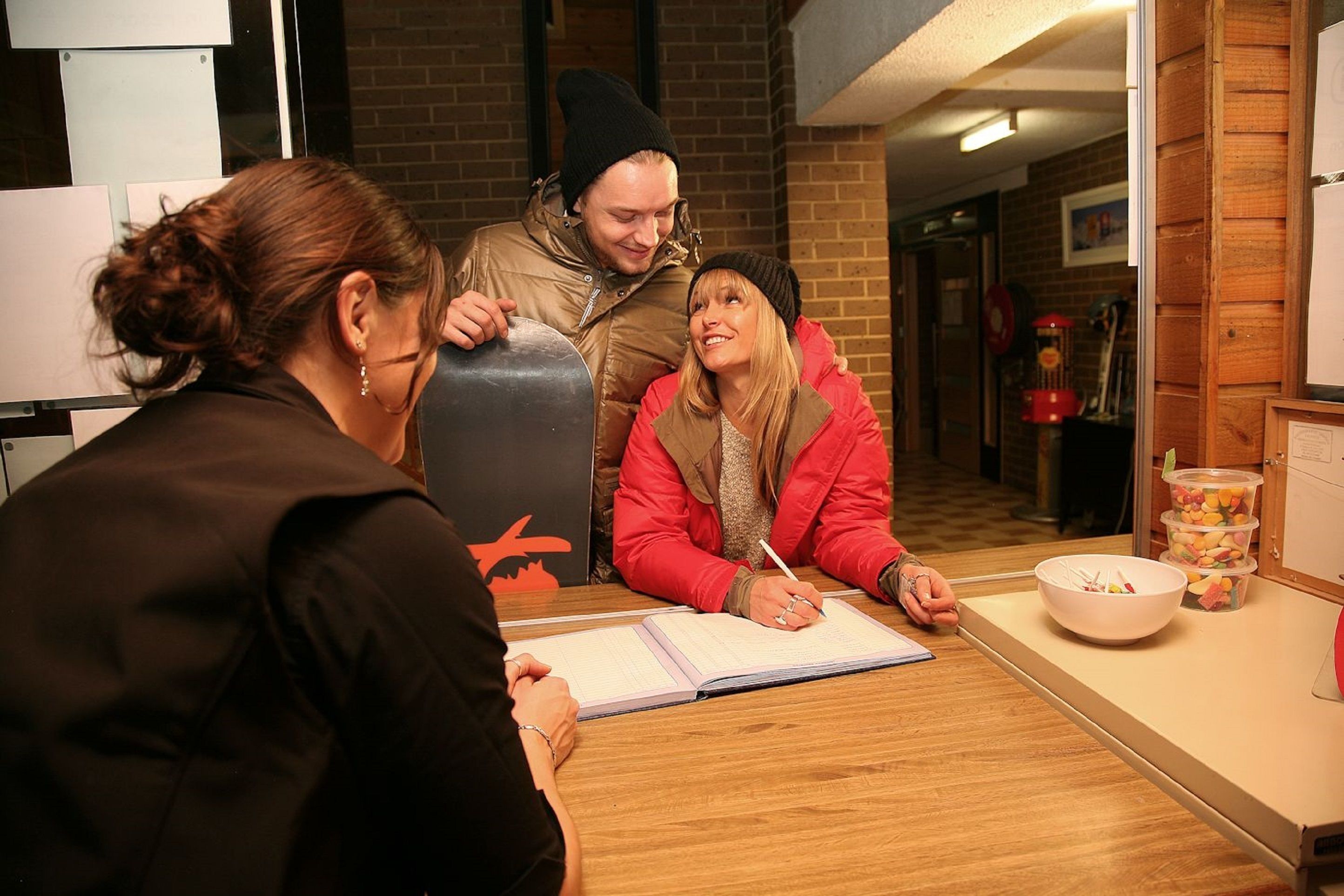 A group of people sitting at a table with a notebook, a pen, and a bowl of snacks.