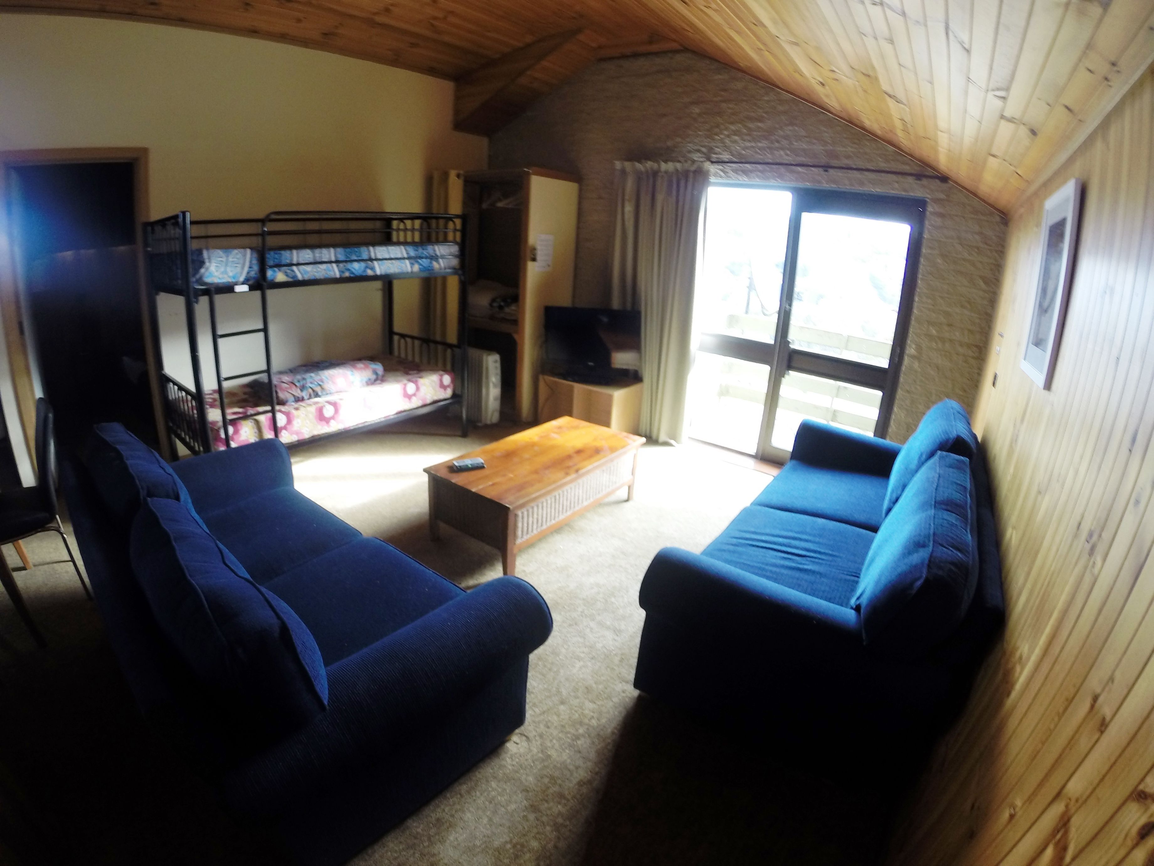 Une pièce chaleureuse avec un lit superposé, deux canapés, une table basse en bois et un téléviseur.