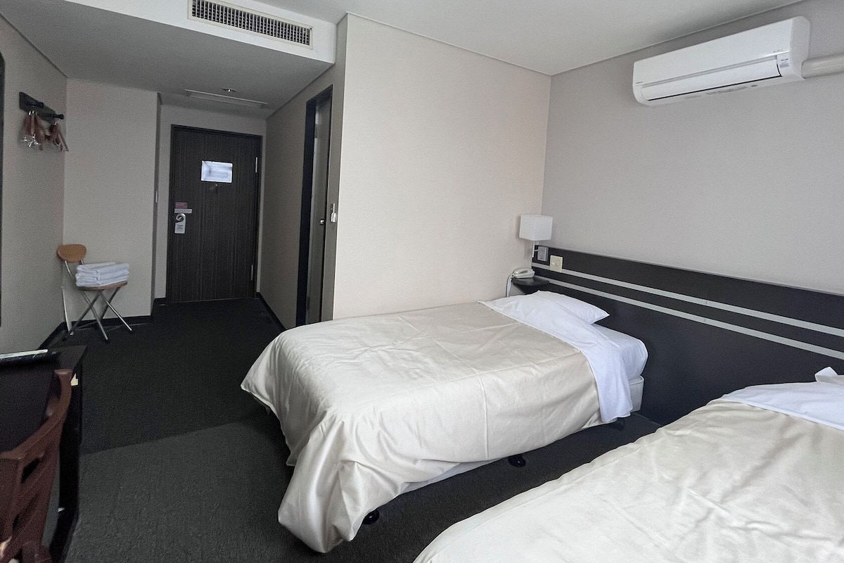 Een hotelkamer met twee bedden, een bureau, een stoel, een kleine tafel en een spiegel.