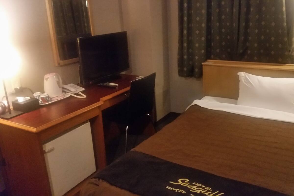 A hotel room with a bed, a desk with a television, a telephone, and a coffee maker.