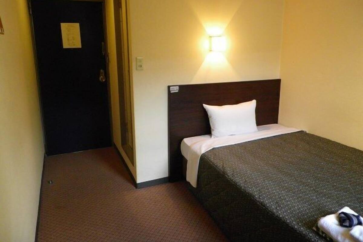 A hotel room with a single bed, a nightstand, a wall-mounted light, and a door leading to another room.