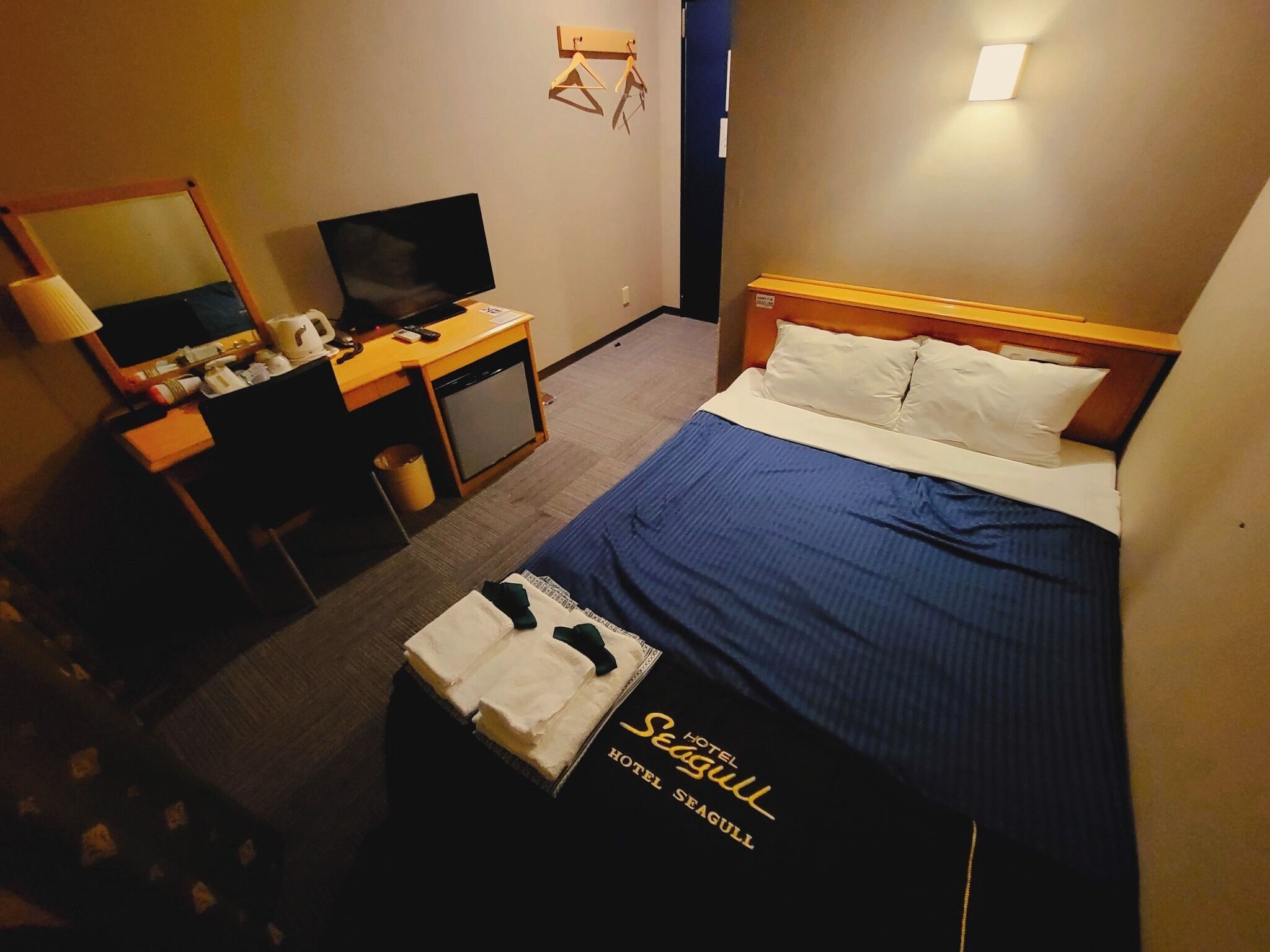 Una habitación de hotel con cama, escritorio, televisor y un mueble pequeño.