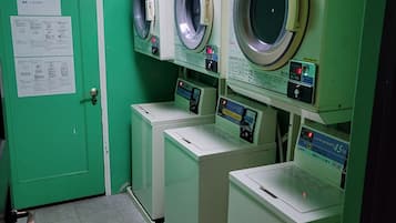Un lavadero con varias lavadoras y secadoras, paredes verdes y una puerta con un letrero.