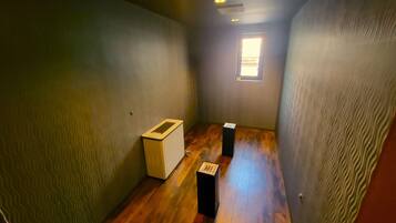 A narrow hallway with wooden flooring, a small window at the end, and two black boxes on the floor.