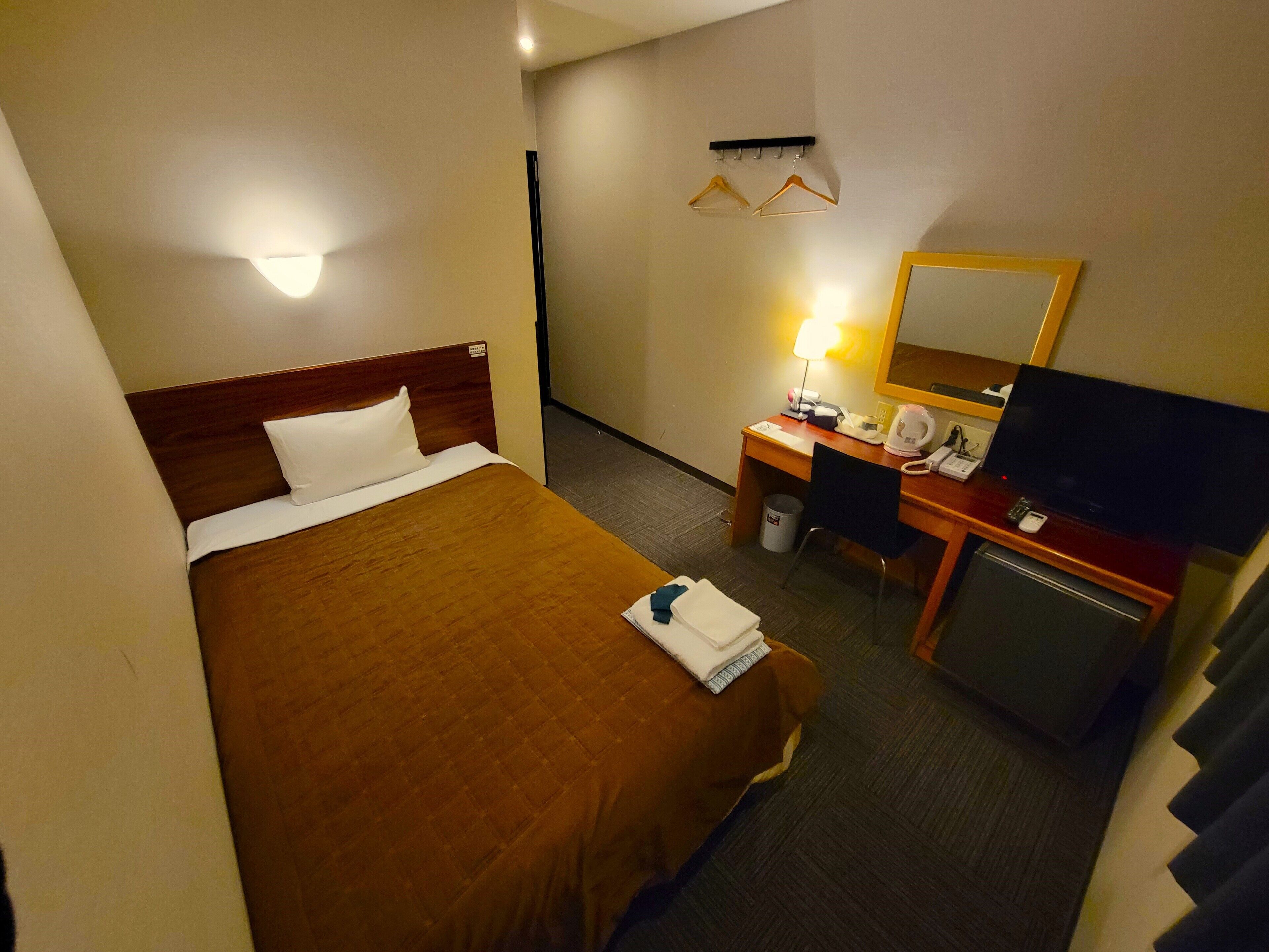 Une chambre d’hôtel équipée d’un lit, d’un bureau, d’une chaise, d’une télévision et d’un miroir.