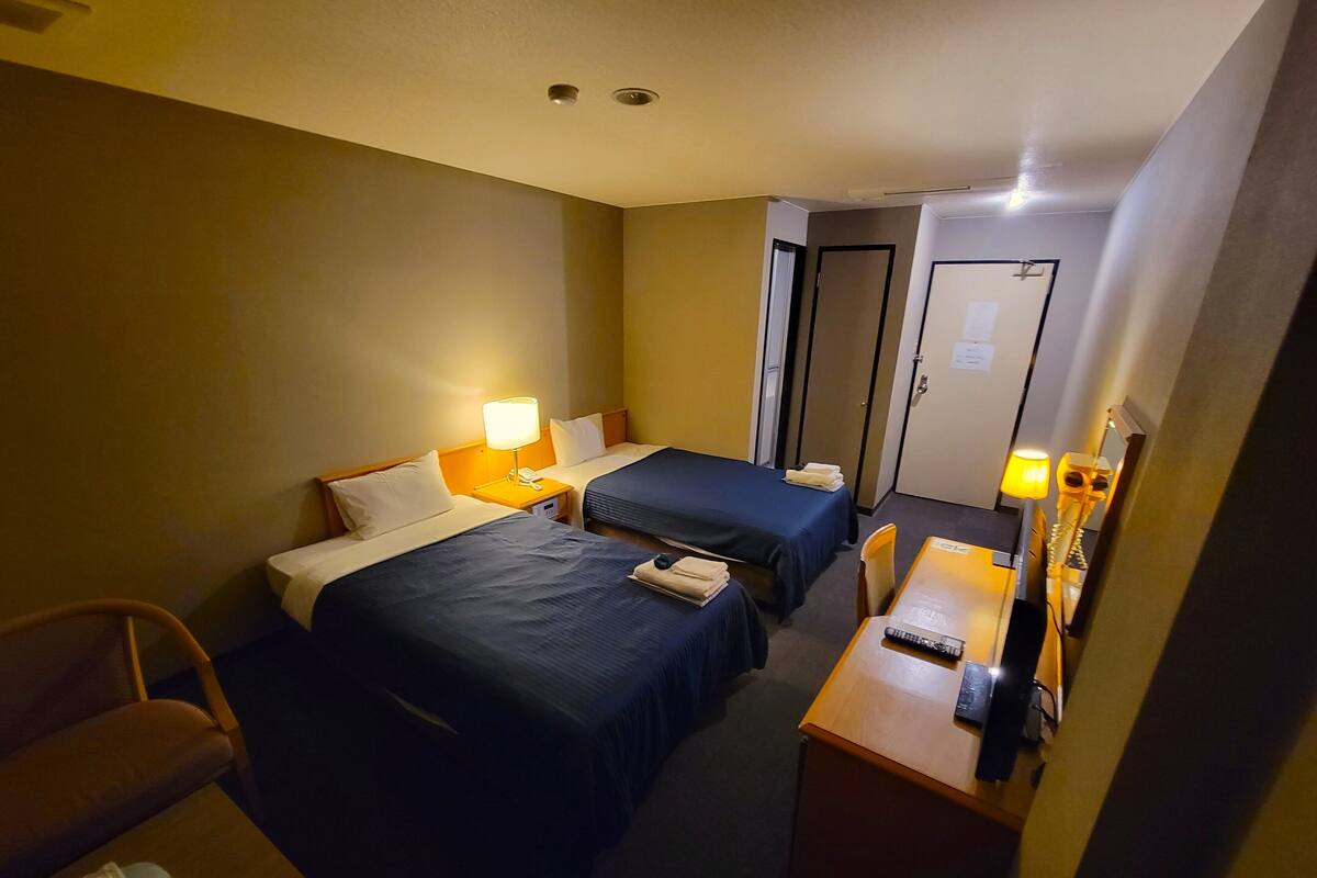 A hotel room with two beds, a desk, a chair, a mirror, and a door.