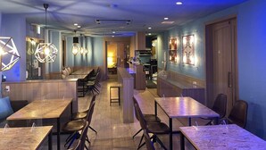 Un restaurante moderno con una decoración en tonos azul y madera, que incluye una zona de bar, mesas de comedor e iluminación contemporánea.