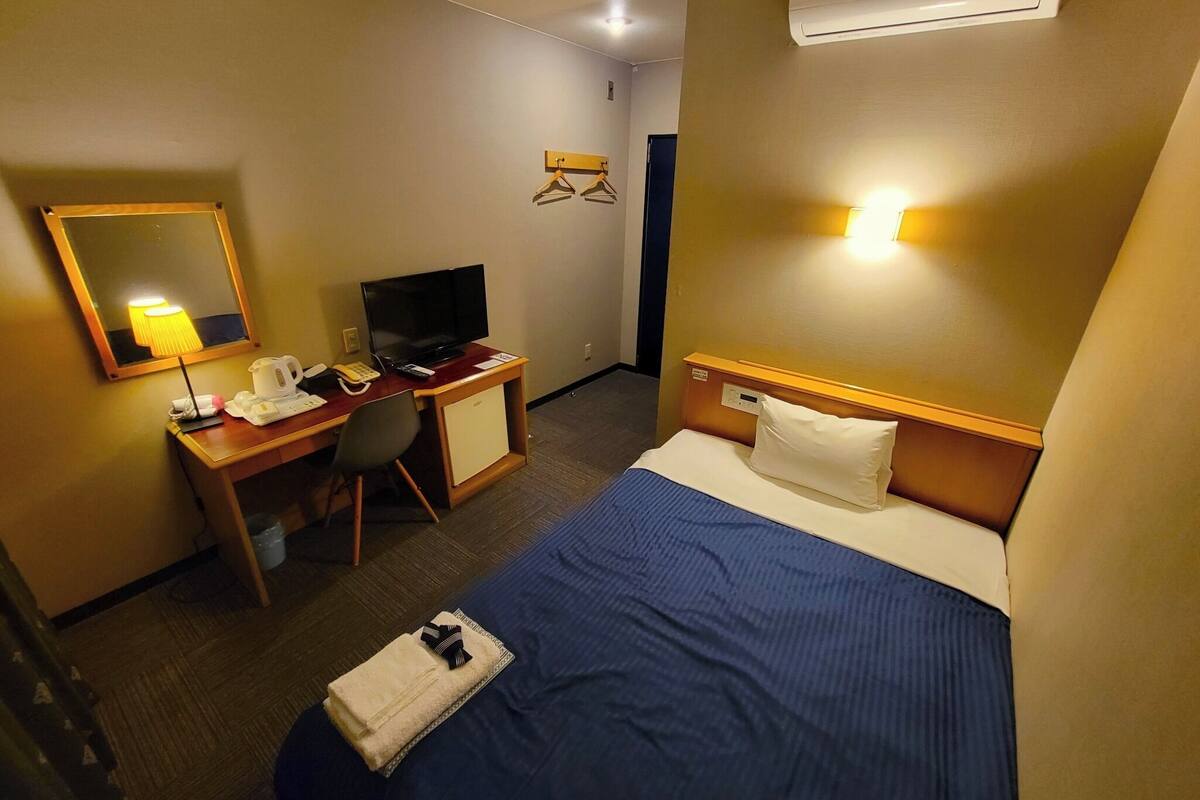 Une chambre d’hôtel comprenant un lit, un bureau avec une télévision, une chaise, une lampe de bureau et un appareil de climatisation.