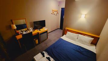 Habitació d'hotel amb un llit, una escriptori amb televisió, un mirall i un petit cubell de paper.