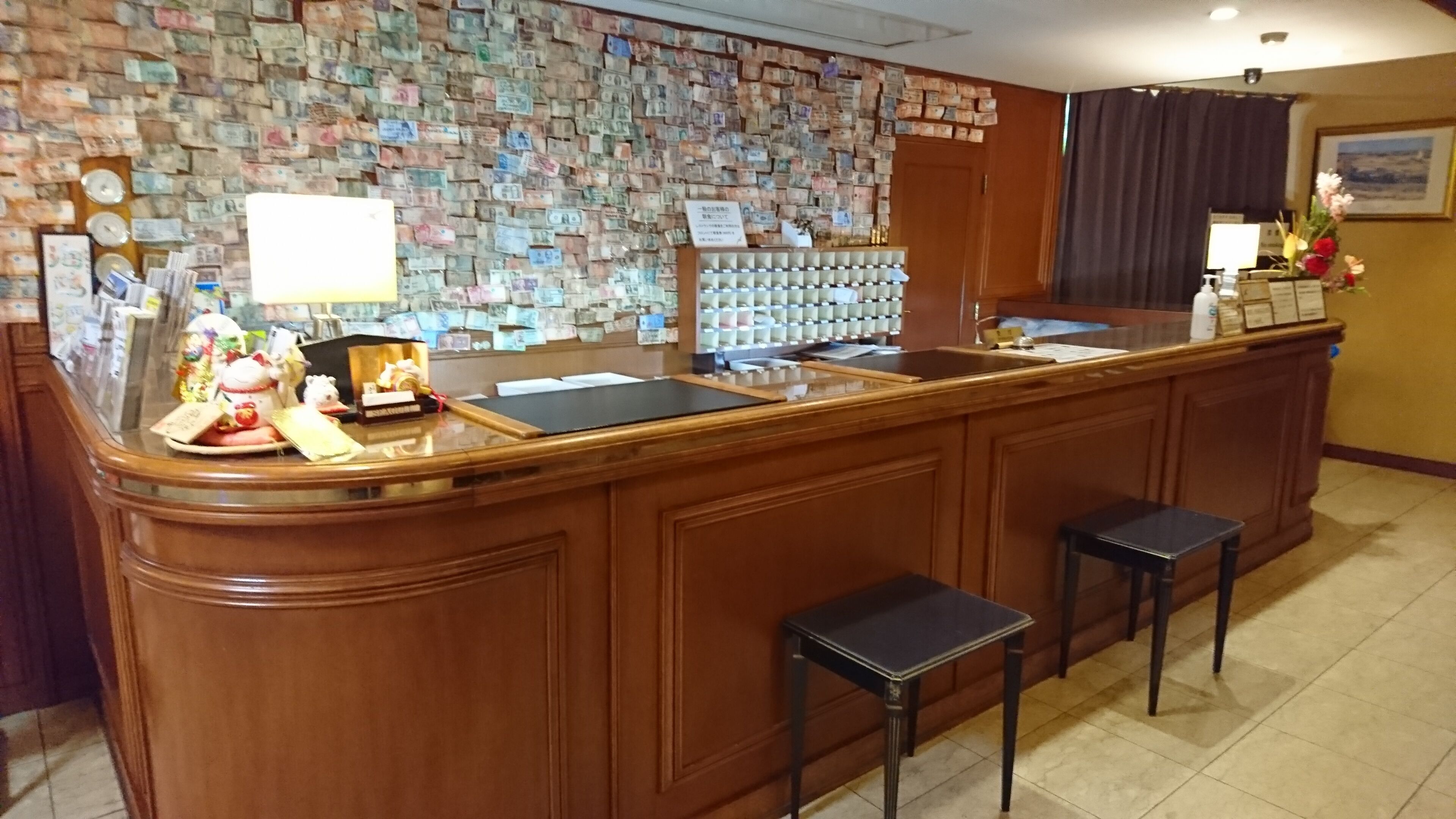A reception area with a wooden counter, a wall covered with currency notes, and a small table with decorative items.