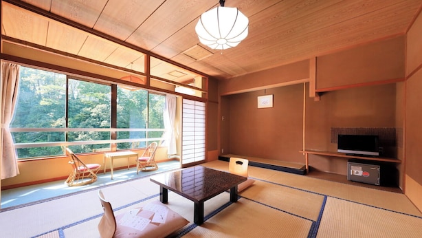 A traditional Japanese room with tatami flooring, a low table, and a television on a shelf. - Ryokan Meisho Tenryukyo Onsen Ryukyotei (Iida)