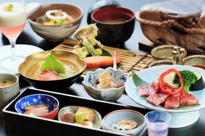 Une variété de plats japonais, notamment des sashimis, des tempuras et des sushis, servis dans de la vaisselle traditionnelle en céramique et en laque.