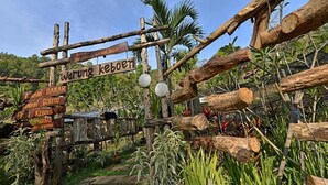 A rustic wooden signpost with multiple directional signs in a garden setting. - Grand Whiz Hotel Trawas (Trawas)