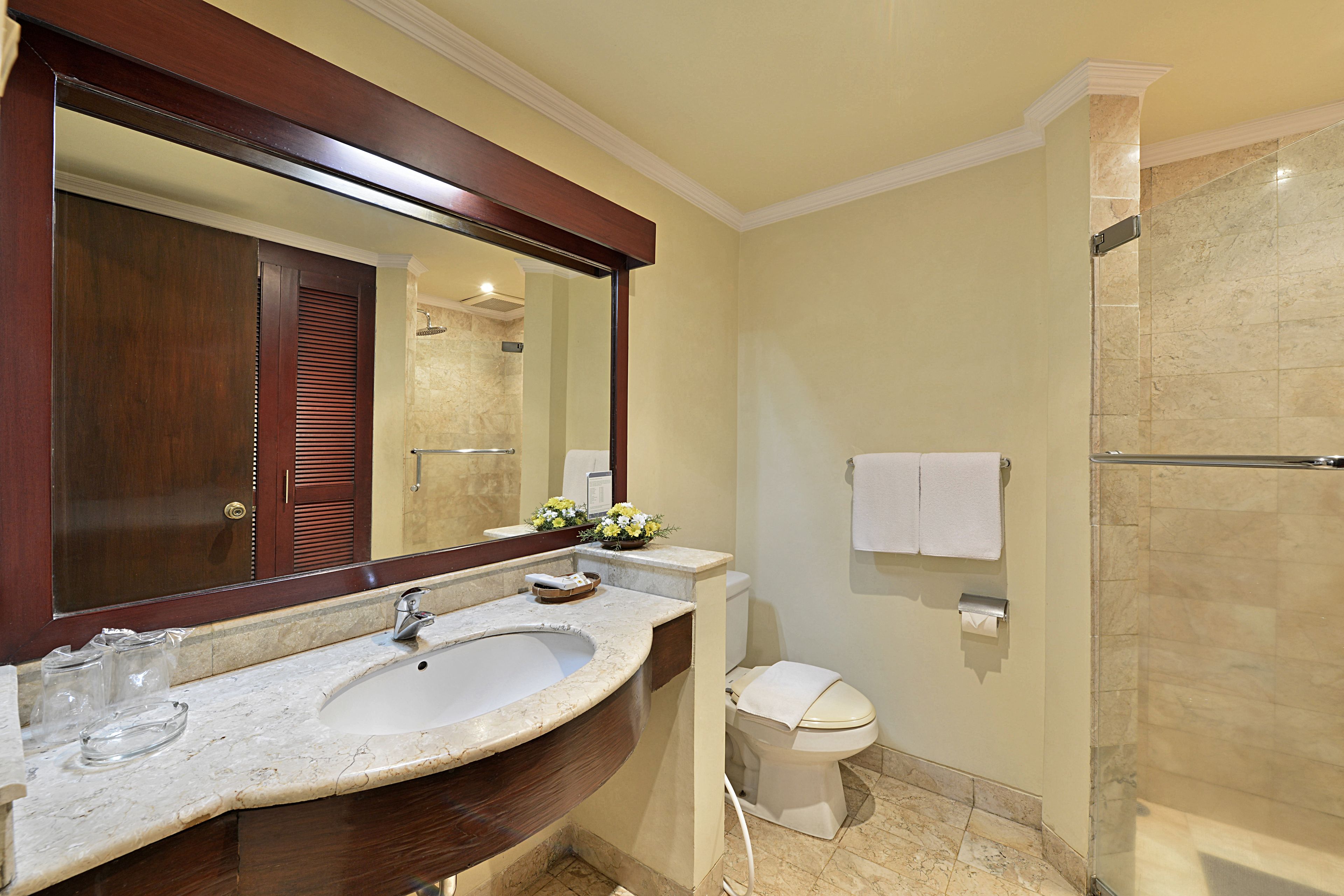 A bathroom with a large mirror, a sink, a toilet, and a shower.
