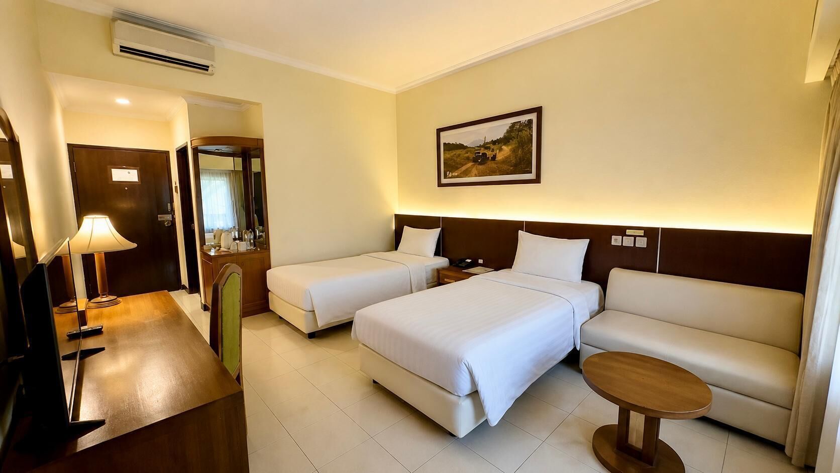 A hotel room with two beds, a sofa, a small table, a TV, and a painting on the wall.