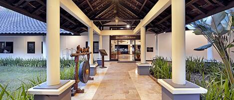 A covered walkway with stone flooring, white pillars, and a sign for the Grand Trawas Hotel.