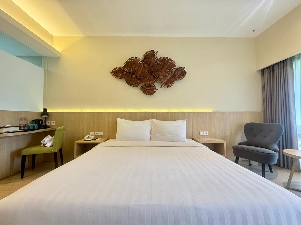 Habitación de hotel con una cama grande, un escritorio, una silla, una mesita de noche y un elemento decorativo en la pared.
