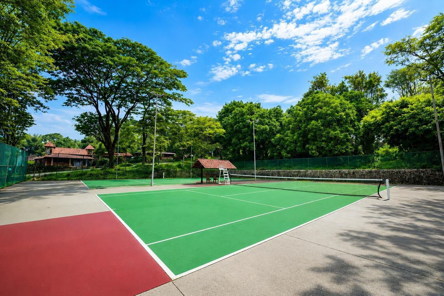 An outdoor tennis court with a green playing surface, a red area, and a pavilion.