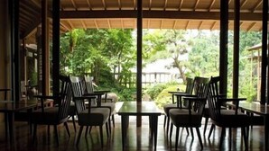 Un espace de restauration intérieur avec des tables et des chaises en bois, de grandes fenêtres et une vue sur la verdure environnante.