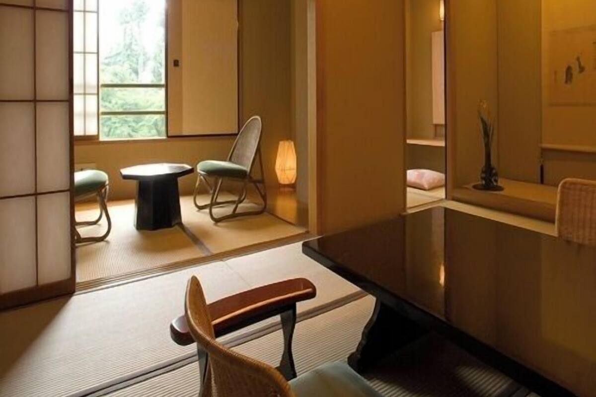 Una habitación tradicional japonesa con suelo de tatami, una mesa baja, una silla y una lámpara colgante.