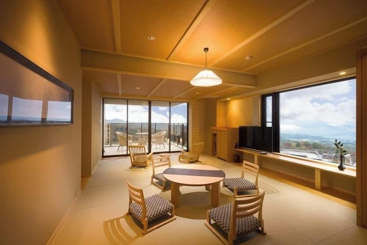 Una sala de estar moderna con una mesa redonda y sillas, un televisor y ventanas amplias con vistas a las montañas.