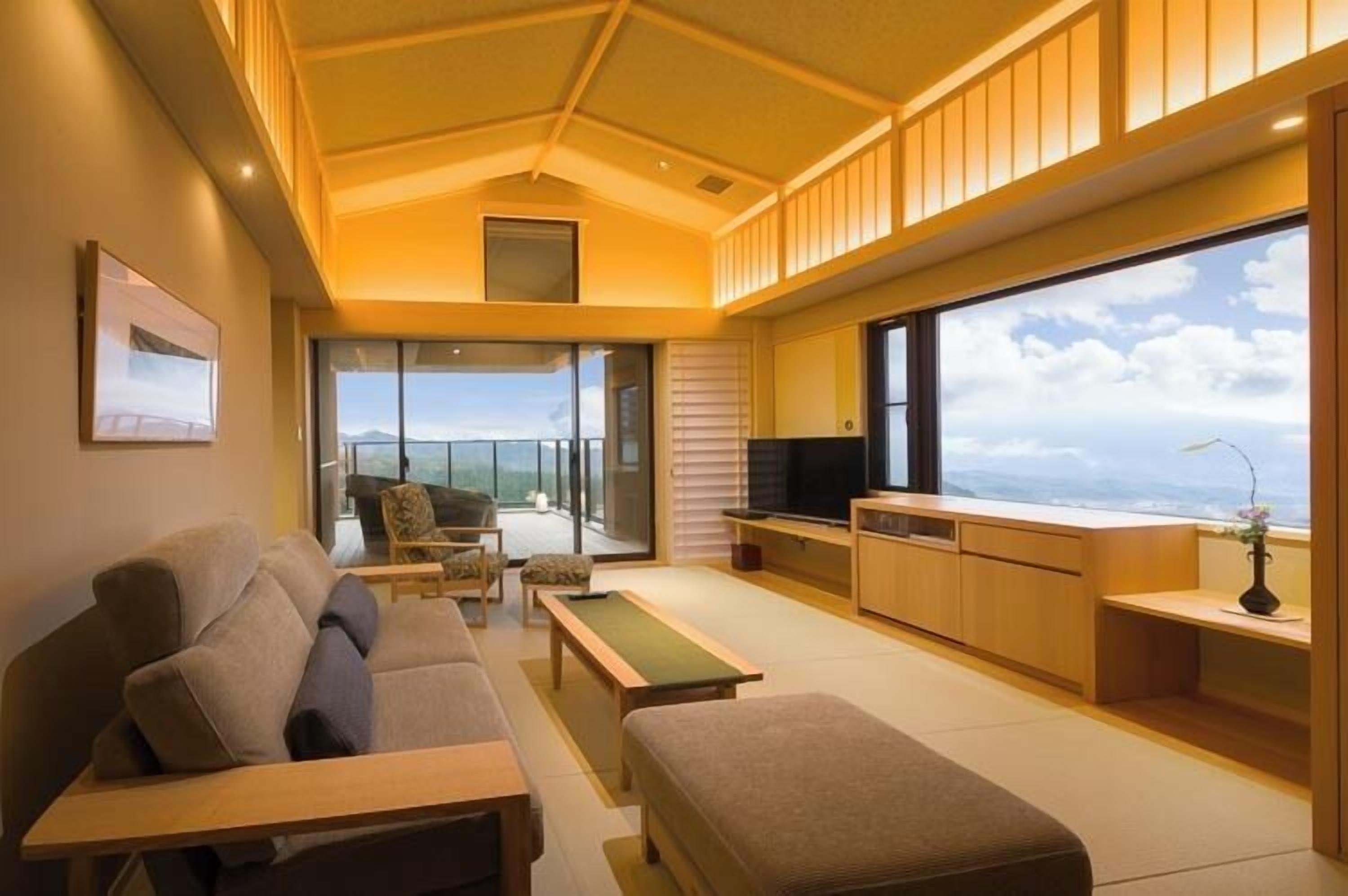 A modern living room with a sofa, a coffee table, a TV, and a balcony with a view.